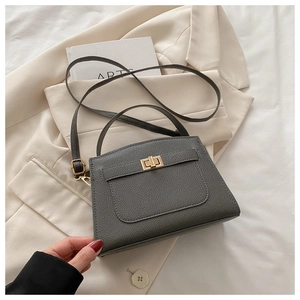 Close-up of grey litchi texture handbag with gold twist lock on beige fabric background