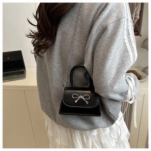 Detail of a black crossbody bag with silver bow decoration and metallic chain strap