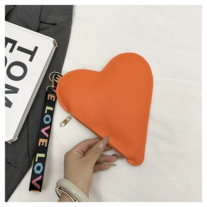 Close-up of heart-shaped orange leather clutch with textured finish and lettered handle strap