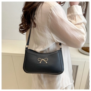 Détail d'un sac sous le bras noir avec boucle nœud doré porté par un mannequin en intérieur