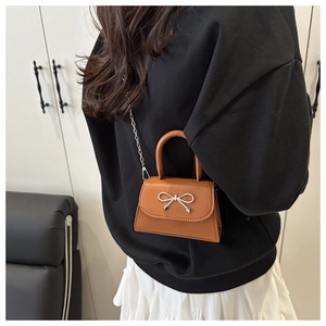 Close-up of brown mini crossbody bag with silver bow ornament and elegant chain strap