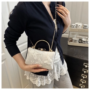 Detailed shot of white floral embroidery lace on a shoulder bag with a gold chain strap