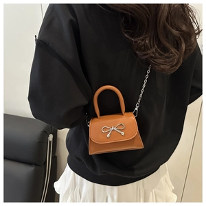 Close-up of orange-brown mini crossbody bag with silver bow ornament and chain strap