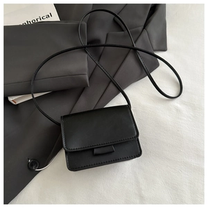 Detailed view of black matte PU leather crossbody bag on white fabric background