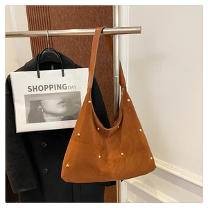 Détail du sac cabas en daim marron avec rivets dorés suspendu sur un support en métal