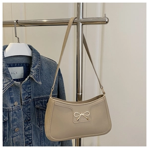 Détail d'un sac hobo beige avec nœud doré sur fond de veste en jean bleu foncé