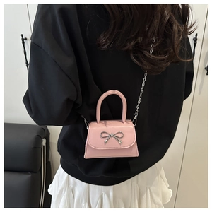 Pink mini crossbody bag with silver bow detail and chain strap shown on a model