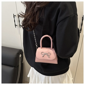 Pink mini square bag with silver bow accent shown on model in a modern interior setting