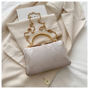Close-up of beige embroidered floral handbag with gold chain and metal handle on beige blazer