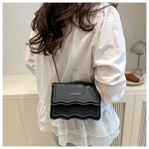 Detail of black pebbled leather crossbody bag with wavy flap and metal chain strap