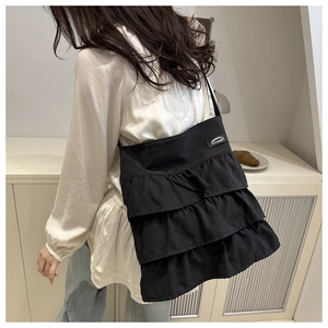 Detail of black tote bag with unique three-layer ruffle design and woven brand label