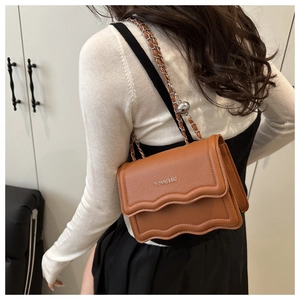 Detail of caramel brown leather bag showing wavy flap design and chain strap with ball adjuster