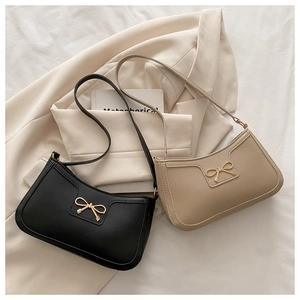 Gros plan de sacs sous le bras noirs et beige avec nœud doré sur un blazer