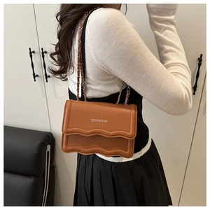 Detail of a brown textured leather crossbody bag with a wavy flap and chain strap