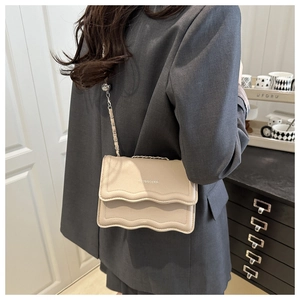 Detailed view of beige crossbody bag with wavy flap, chain strap, and silver orb charm