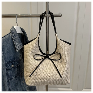 Detail of a beige woven beach tote bag with black bow tie and spacious interior design
