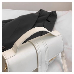 Detail of white leather handbag with gold logo and vertical stitching on the flap