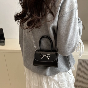 Minimalist black mini crossbody bag with silver bow detail and chain strap on model