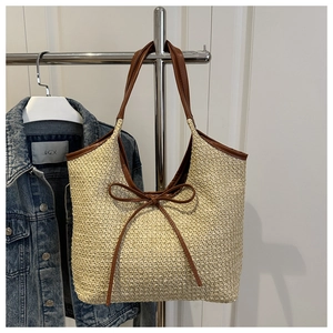 Detail of woven straw beach tote bag featuring decorative brown leather bow and handles