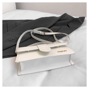 Close-up of a white rectangular crossbody bag with a gold metal logo and precise stitching