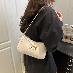 Chic cream white leather underarm bag with gold bow detail worn by model at home