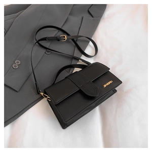 Detail of black leather crossbody bag with gold metal logo on a grey suit jacket