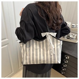 Rear view of striped canvas tote bag with lace bow detail on a shoulder