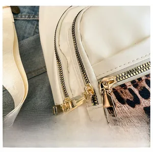 Detailed close-up of smooth gold metal zippers on white leather bag with leopard print accent