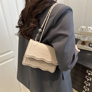 Chic beige crossbody bag with wavy edge design and elegant metal chain strap