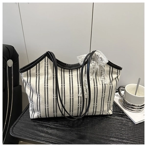 Close-up of black and white striped canvas tote bag with leather straps and lace bow
