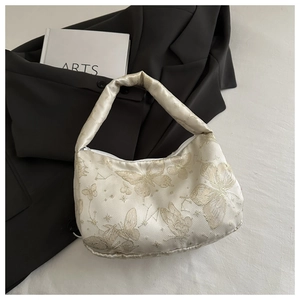 Vue détaillée de la broderie papillon sur un sac crème posé sur un blazer noir