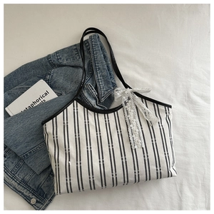 Detail of canvas tote bag featuring vertical stripes, black piping, and lace bow accent