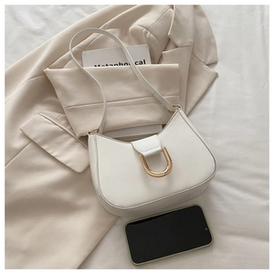 Close-up of a white crescent shoulder bag featuring a prominent gold horseshoe buckle