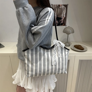 Striped canvas tote bag with lace bow accessory shown in a casual lifestyle setting