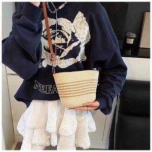 Détail du sac seau en paille tissé main avec rayures brunes et bandoulière en cuir