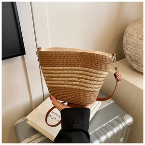 Détail du sac seau en paille tissée avec motif rayé et bandoulière en cuir marron