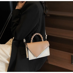 Detail view of woven top handle and gold trim on beige contrast flap handbag