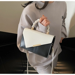 Detail of contrast woven handle and gold metal buckle on a black and white crossbody bag