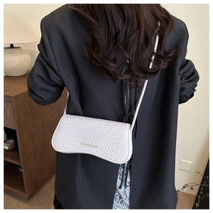 Detail view of a white crocodile texture underarm bag on a black blazer outfit