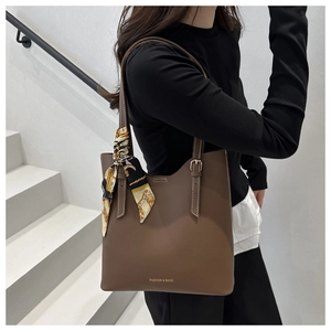 Detail of a large brown leather tote bag with a geometric scarf on a model's shoulder