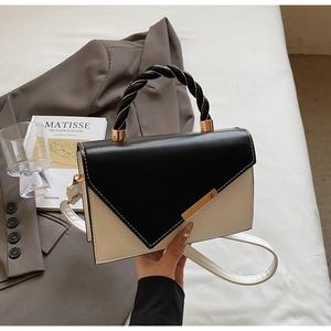 Detail of two-tone crossbody bag with black envelope flap and gold metal bar decoration