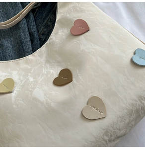 Detail of cream glossy wrinkled fabric with colorful sewn heart patches on a stylish tote