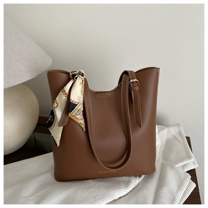 Close-up of brown leather tote bag with decorative silk scarf and fashion text logo