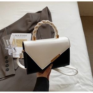 Detail view of contrast color handbag with twisted woven handle and gold metal clasp
