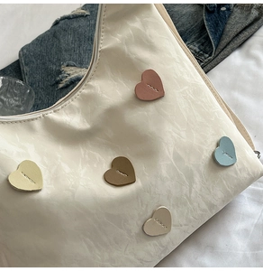 Detailed view of white crescent bag featuring five colorful heart patches and crinkle texture