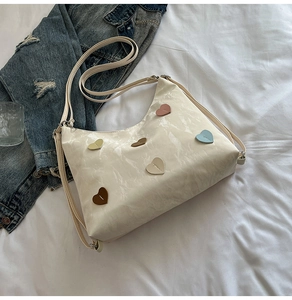Detail view of cream hobo bag with colorful heart patches and adjustable shoulder strap