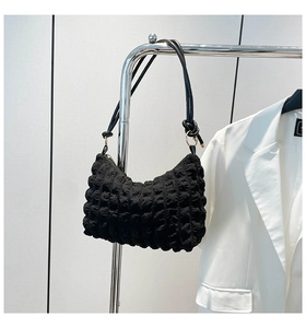 Detail of black bubble textured handbag with knotted shoulder strap and gold hardware