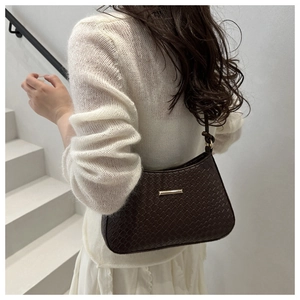 Detail of dark brown woven leather underarm bag with gold metal hardware on model