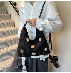 Detail of black pleated leather tote bag featuring five colorful heart patches