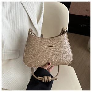 Detail of beige woven texture shoulder bag with gold metal buckle and knotted strap
